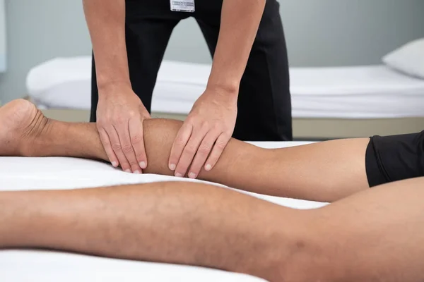 理学療法士は 医療室のベッドで横たわる患者の脚のハンドルを使ってください — ストック写真