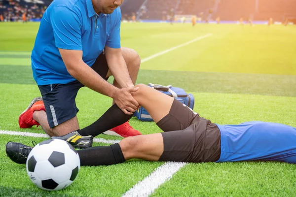 Mavi bir gömlek, siyah pantolon içinde çim yarış sırasında yaralı giyen futbolcu.