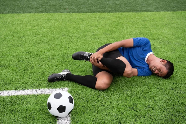 Mavi bir gömlek, siyah pantolon içinde çim yarış sırasında yaralı giyen futbolcu.