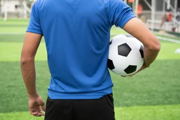 Siyah futbol topu tutan mavi bir gömlek giymiş futbolcu.