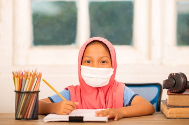 Okul konseptine dönersek, evde çalışan Müslüman kızlar sosyal mesafeyi azaltmak ve bulaşıcı hastalıkları önlemek için hijyenik maskeler takıyorlar.