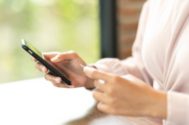 Kafe alışverişinde cep telefonuyla ameliyat maskesi takan bir kadın.