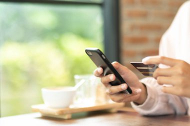 Kafe alışverişinde cep telefonuyla ameliyat maskesi takan bir kadın.