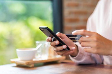 Kafe alışverişinde cep telefonuyla ameliyat maskesi takan bir kadın.