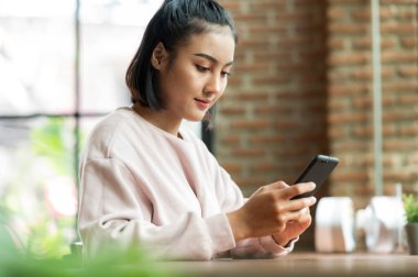 Kafe alışverişinde cep telefonuyla ameliyat maskesi takan bir kadın.