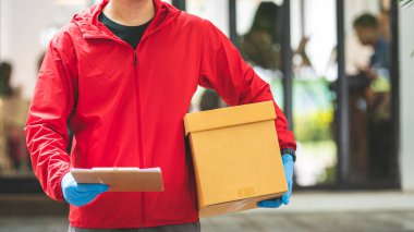 Teslimatçı adam kırmızı eldiven giymiş, elinde karton kutular var.
