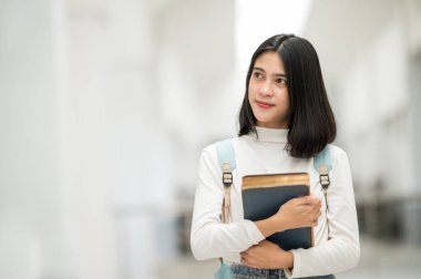 Asyalı bir kız üniversite öğrencisi üniversiteye gülümsedi ve kameraya baktı..