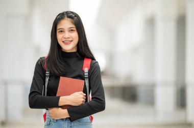 Asyalı bir kız üniversite öğrencisi üniversiteye gülümsedi ve kameraya baktı..