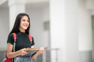 Asyalı bir kız üniversite öğrencisi üniversiteye gülümsedi ve kameraya baktı..