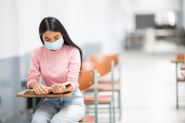 Üniversite bayan öğrencileri bulaşıcı hastalıkları önlemek için Sosyal Mesafe sınıfında oturuyorlar.