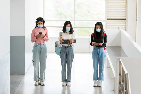 A female college student wearing a mask stands at social distances at the university.