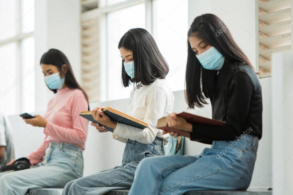 A group of students wearing masks sitting at the university reading.