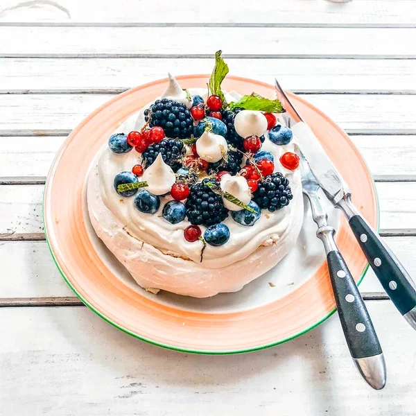 Gourmet pavlova cake with fresh berry topping and layers of whipped cream and meringue served on a plate with a spatula in a close up view