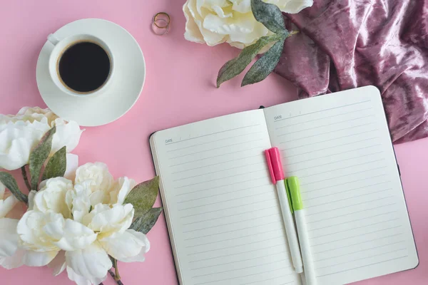 Bir fincan kahve ve çiçekli pembe arka plan üstünde defter