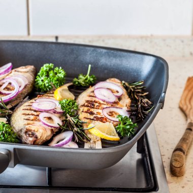 Gaz ocağının tepesindeki tavada ızgara Breams, kare.