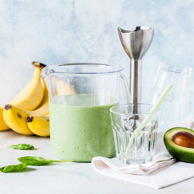 Sağlıklı yeşil meyve püresi Avokado, Muz ve Ispanak 'tan alınmış bir ölçü kabında el blenderiyle harmanlanmış.