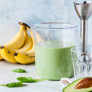 Sağlıklı yeşil meyve püresi Avokado, Muz ve Ispanak 'tan alınmış bir ölçü kabında el blenderiyle harmanlanmış.