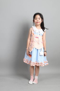 Gri arka planda duran, süslü giyinmiş Asyalı küçük kız..