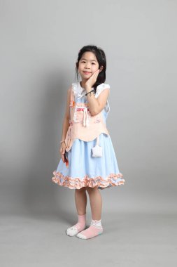 Gri arka planda duran, süslü giyinmiş Asyalı küçük kız..