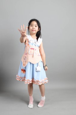 Gri arka planda duran, süslü giyinmiş Asyalı küçük kız..