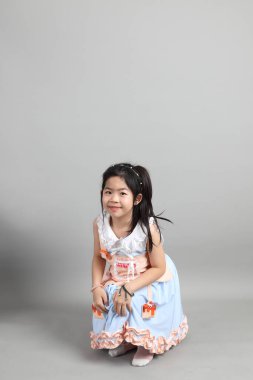 Gri arka planda duran, süslü giyinmiş Asyalı küçük kız..