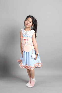 Gri arka planda duran, süslü giyinmiş Asyalı küçük kız..