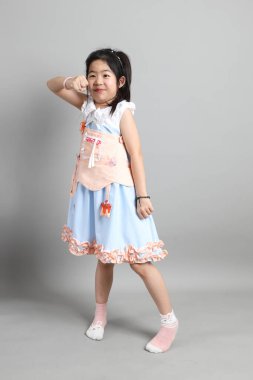 Gri arka planda duran, süslü giyinmiş Asyalı küçük kız..