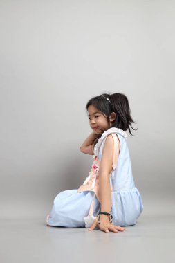Gri arka planda oturan süslü giyinmiş Asyalı küçük kız..