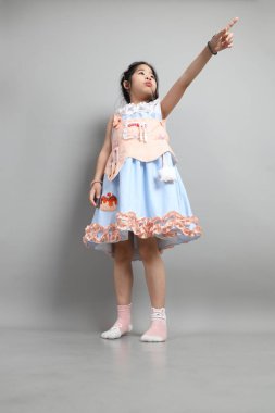 Gri arka planda duran, süslü giyinmiş Asyalı küçük kız..