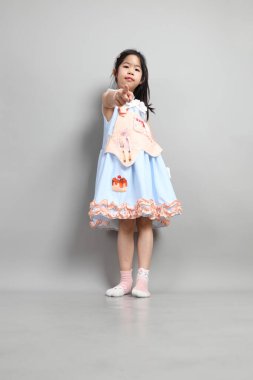 Gri arka planda duran, süslü giyinmiş Asyalı küçük kız..