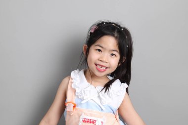 Gri arka planda duran, süslü giyinmiş Asyalı küçük kız..