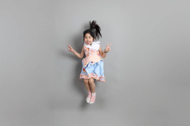 Gri arka planda duran, süslü giyinmiş Asyalı küçük kız..