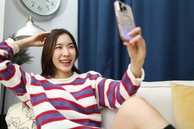 Doğu Asyalı kadın evinde akıllı telefon kullanıyor oturma odasında..