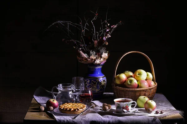 Vintage village still life : autumn leaves in a clay vase, basket of apples, pie, silver knife, antique tea cup, jar, glass of wine, hazelnuts, walnuts and chestnut on a table in light and shadows. Royalty Free Stock Images