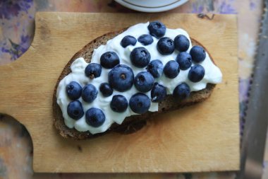 Çavdar ekmeği ile yoğurt ve yaban mersini bir ahşap tahta üzerinde bir parça. Sağlıklı Kahvaltı, kahve molası, vintage nostaljik atmosferde, doğal gıda. Litvanya geleneksel karanlık ekmek. Düz yatıyordu.