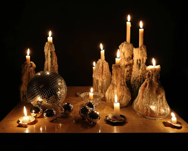 Ano Novo ainda vida: queimando velas em garrafas de vidro, castiçais de cristal e conchas do mar, bola de espelho, decorações de Natal de prata em uma mesa no escuro. Cera derretida, chamas, luzes, brilhos . — Fotografia de Stock