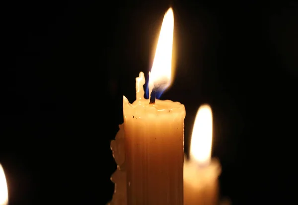 Nahaufnahme brennender Wachskerzen im Dunkeln. Kerzenflamme, Kerzendocht. Weihnachten, Neujahr, Grußkarte, Allerheiligen, Heiliger Abend, Kirche, Religion, Glaube, Gebet, Feiertag, Magie. — Stockfoto