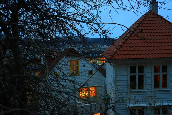 Vista de Bergen, Noruega al atardecer. Casas tradicionales de madera blanca con techos de tejas rojas, ramas de árboles, linternas. Paisaje urbano en el fondo . — Foto de Stock