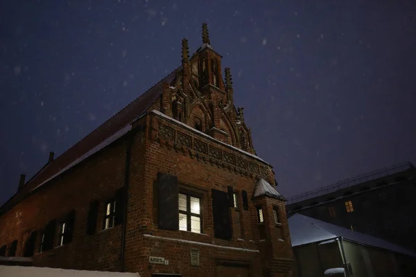 Vista de la famosa casa gótica medieval de Perkunas en el casco antiguo de Kaunas en una noche nevada de invierno. Monumento histórico de Lituania. Europa atracción turística . — Foto de Stock