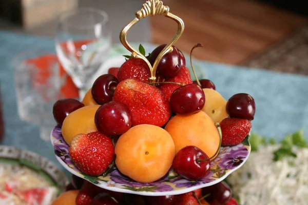 Fruit plate with strawberry, apricot and cherry on violet plate on a festive table on the background of a kitchen interior