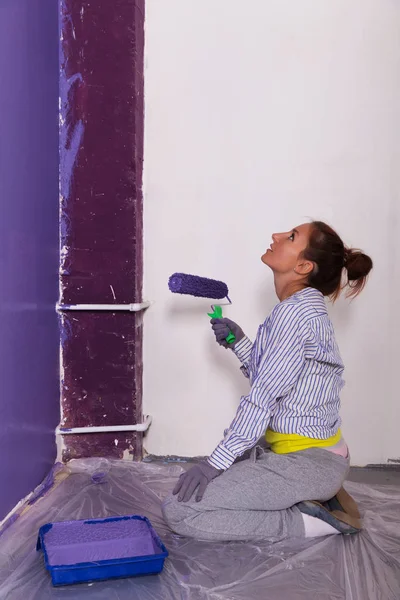 Ung attraktiv kvinna målar vit vägg med lila färg rolle — Stockfoto