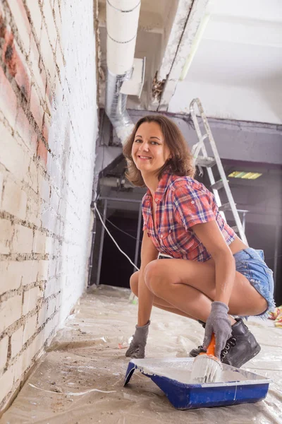 Ung attraktiv kvinna målar vitt tegel vägg och pensel — Stockfoto