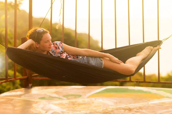 Jonge slanke vrouw in tropische exotische hangmat zonsondergang verlichting — Stockfoto