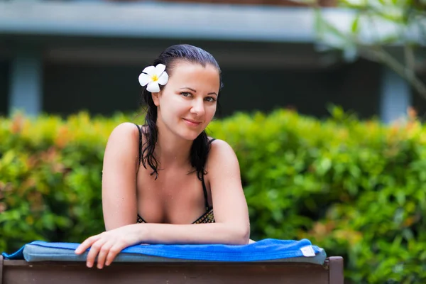 Young woman gets suntan near tropical swimming pool in bikini — Stock Photo, Image