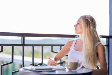 Genç kadın kahve içmek ve Not defteri günlüğü kafede masada yazma