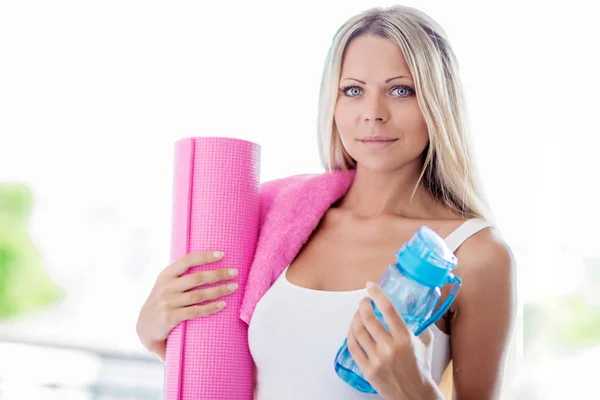 Young blonde woman going fitness sport with towel, bottle of water and pink yoga mat