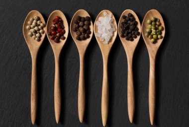 Biber ve tuz tahta kaşıklar siyah arduvaz arka plan üzerinde farklı tür