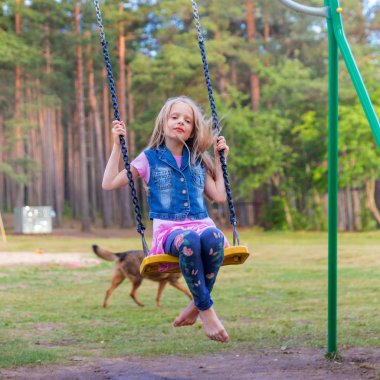 Açık havada bir oyun alanı üzerinde sallanan küçük sarışın kız