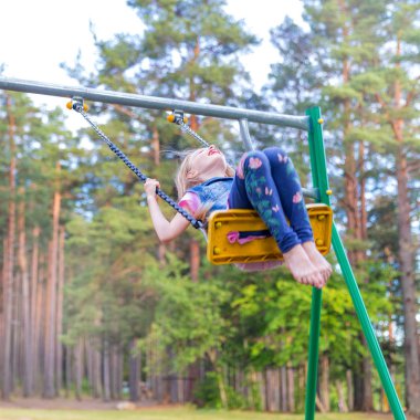 Açık havada bir oyun alanı üzerinde sallanan küçük sarışın kız