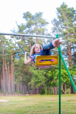 Açık havada bir oyun alanı üzerinde sallanan küçük sarışın kız